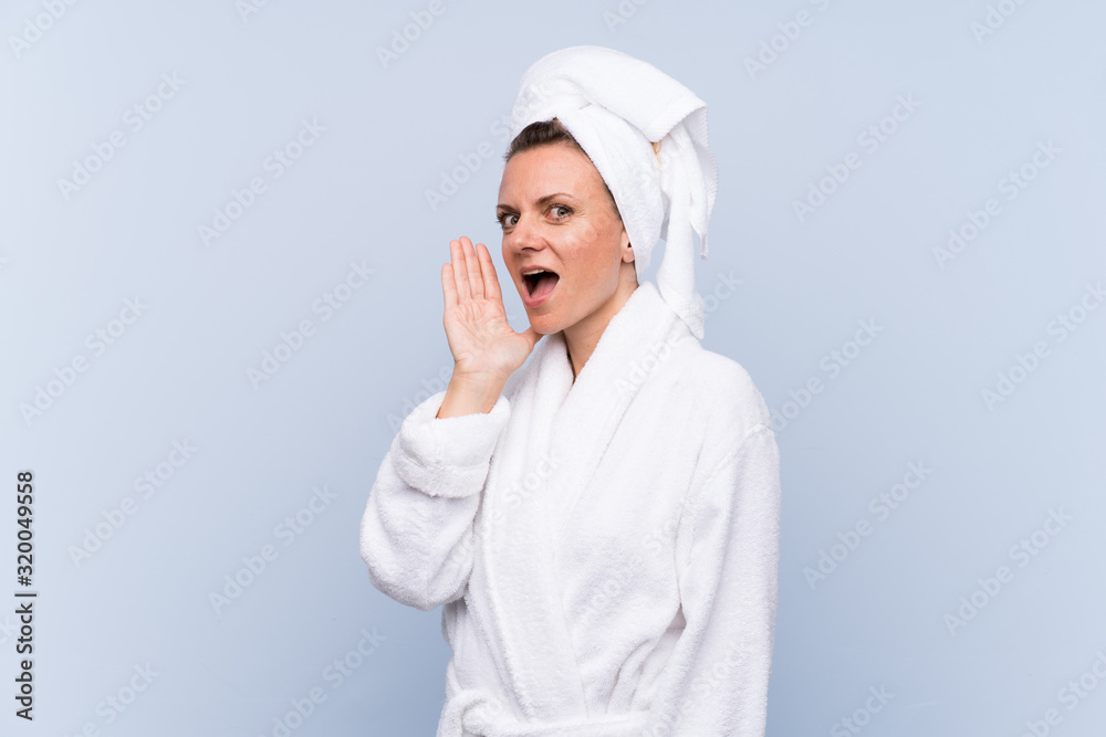 Woman in bathrobe over isolated blue background shouting with mouth wide open Woman in bathrobe over isolated blue background shouting with mouth wide open