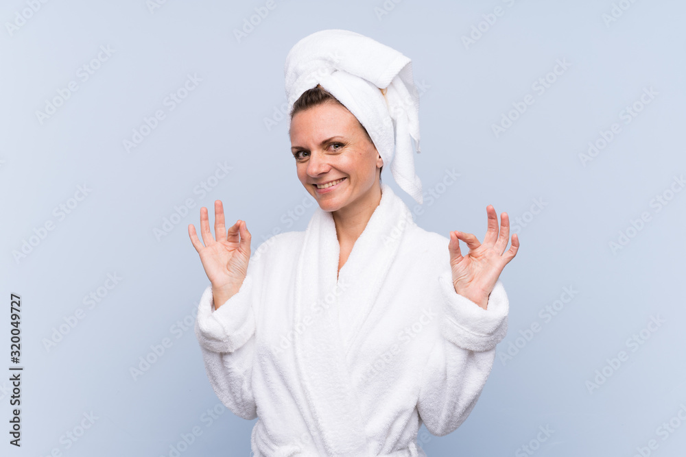Woman in bathrobe over isolated blue background showing an ok sign with fingers Woman in bathrobe over isolated blue background showing an ok sign with fingers