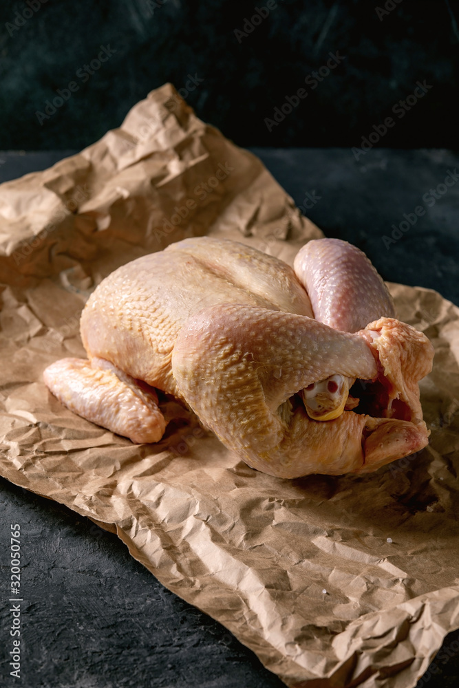Whole raw organic uncooked farmer chicken poultry on crumpled craft paper over black concrete background. Copy space