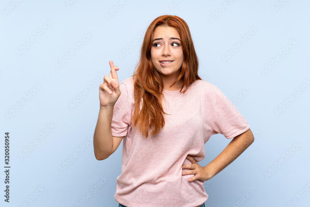 Teenager redhead girl over isolated blue background with fingers crossing and wishing the best Teenager redhead girl over isolated blue background with fingers crossing and wishing the best