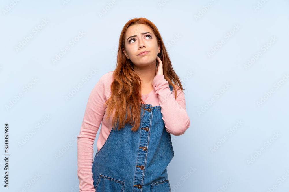 Teenager redhead girl with overalls over isolated blue background thinking an idea Teenager redhead girl with overalls over isolated blue background thinking an idea