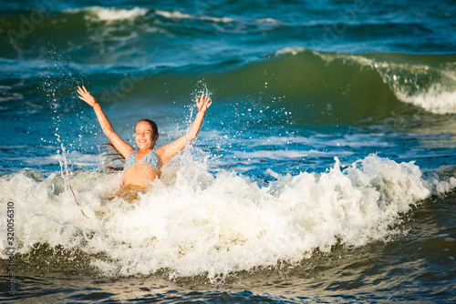 Emotional active little girl splashing in the stormy sea waves on a sunny summer day during the holidays. The concept of family holidays with children. Lovers of water and the elements