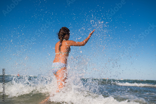 Little funny active happy girl splashing in the noisy sea waves on a sunny warm summer day. Sea vacation concept with kids. Advertising space © YouraPechkin