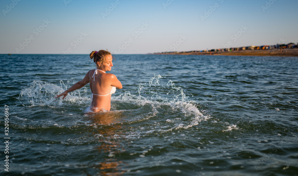 Beautiful cheerful young woman bathes in water and rejoices raising her hands up on sunny warm summer evening. Concept of enjoying a long-awaited vacation. Copyspace Beautiful cheerful young woman bathes in water and rejoices raising her hands up on sunny warm summer evening. Concept of enjoying a long-awaited vacation. Copyspace