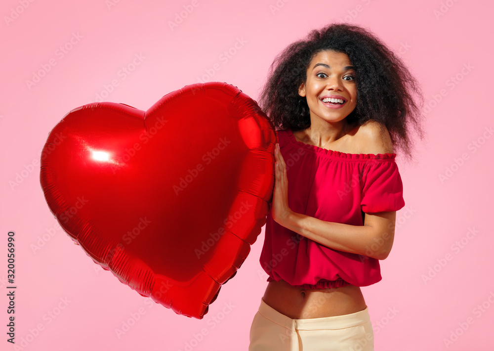 Happy girl holds red heart shape balloon. Photo of smiling young girl in love on pink background. Valentine's Day Happy girl holds red heart shape balloon. Photo of smiling young girl in love on pink background. Valentine's Day