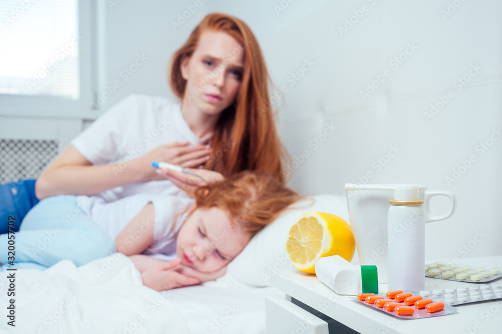 redhaired ginger worried woman checking temperature of her sick little daughter