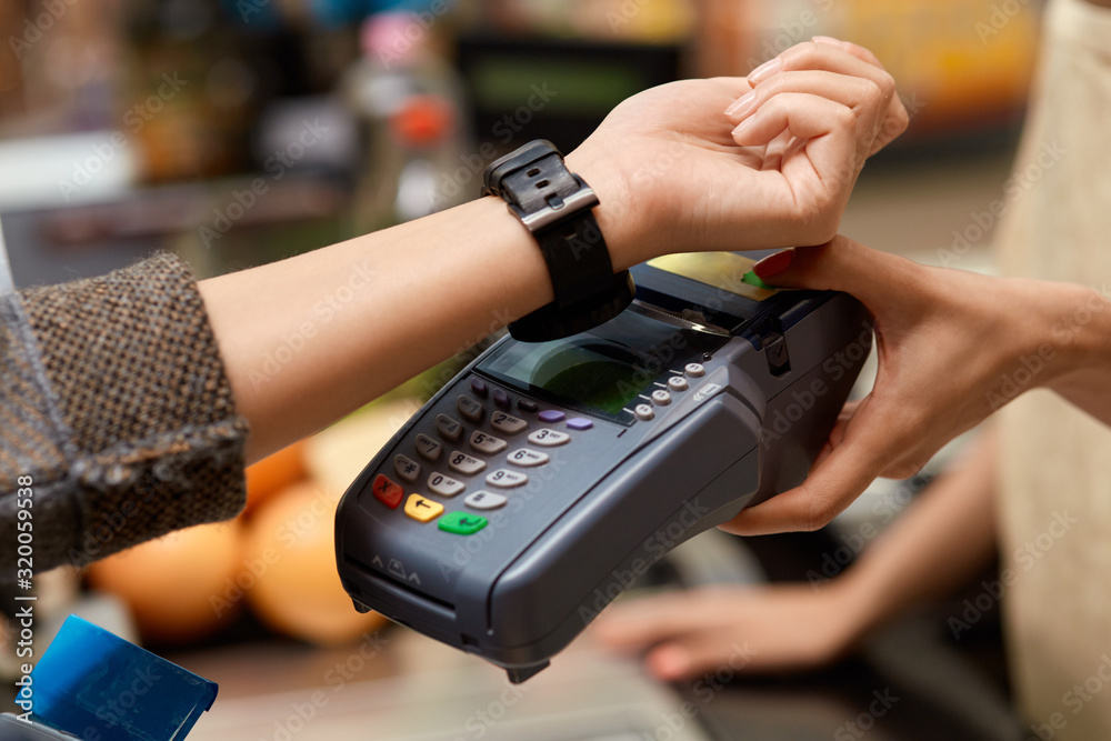 Daily Shopping. Woman standing at the supermarket cashier counter paying for purchases contactless with smartwatch close-up