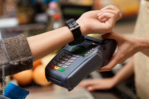 Daily Shopping. Woman standing at the supermarket cashier counter paying for purchases contactless with smartwatch close-up © Viktoriia