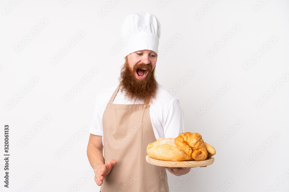 Redhead man in chef uniform. Male baker holding a table with several breads with surprise and shocked facial expression Redhead man in chef uniform. Male baker holding a table with several breads with surprise and shocked facial expression