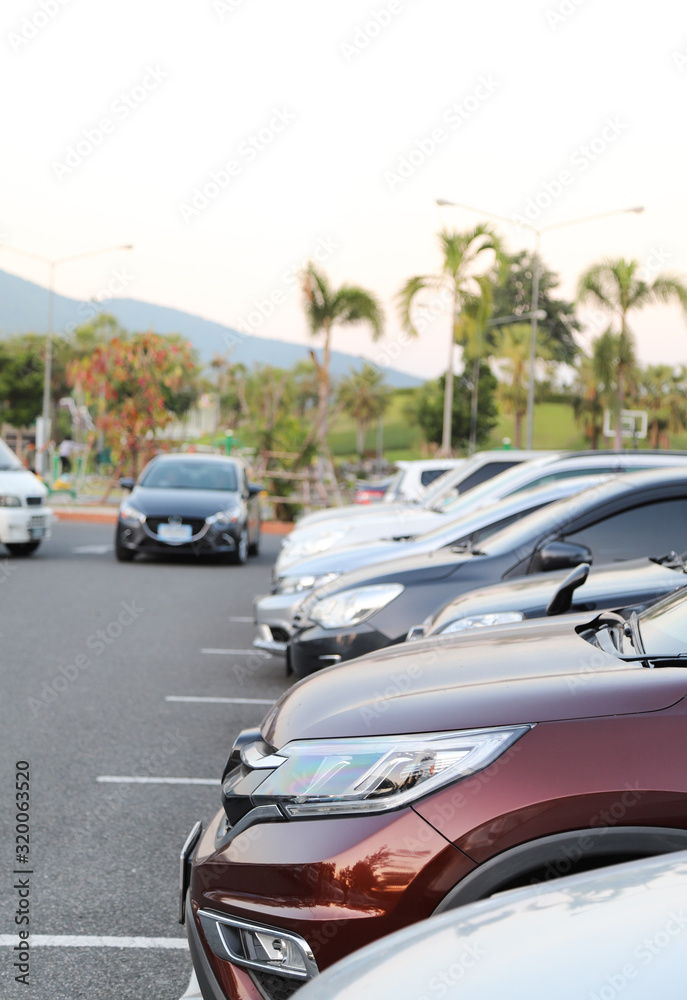 Closeup of front side of dark red  car and other cars parking in outdoor parking lot with natural background in twilight evening. Vertical view.