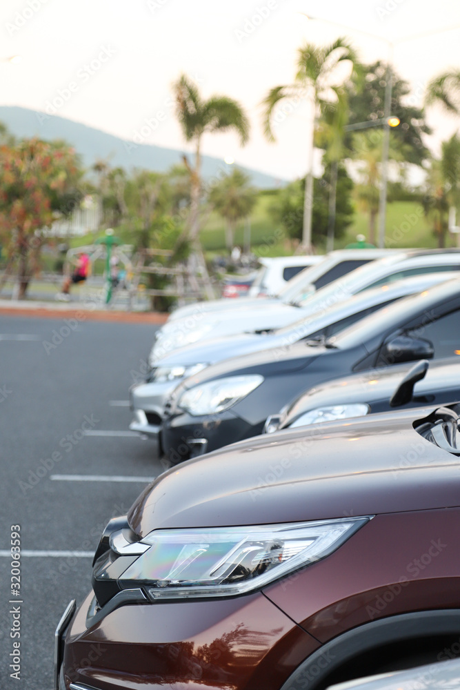 Closeup of front side of dark red  car and other cars parking in outdoor parking lot with natural background in twilight evening. Vertical view.