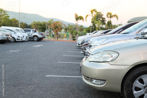 Closeup of front side of golden car and other cars parking in outdoor parking lot with natural background in twilight evening. 