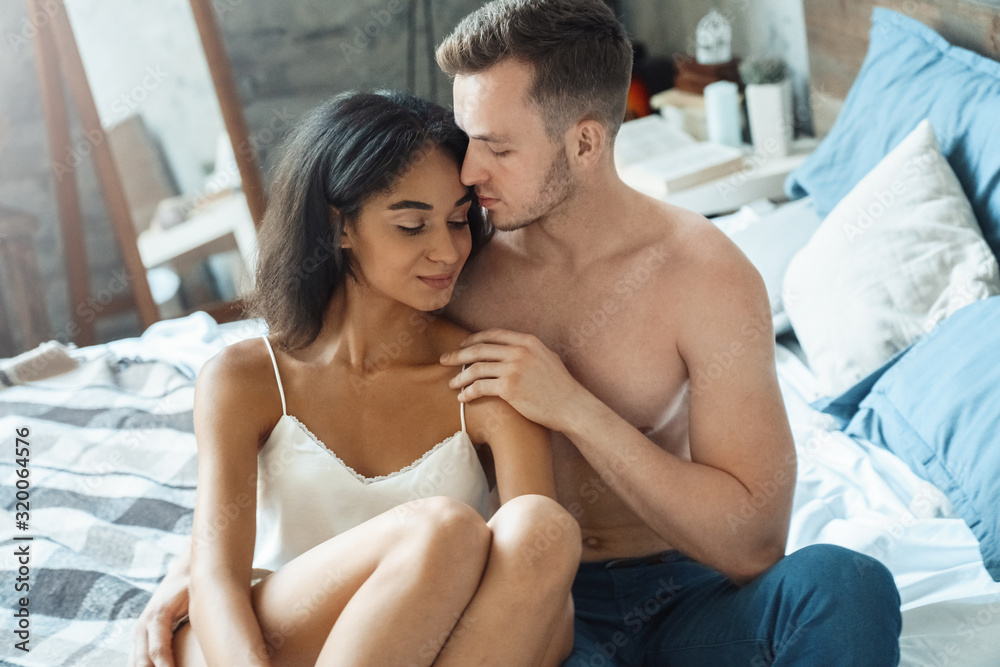Mixed Race Couple. Young man and woman in bedroom sitting on bed touching each other tender Mixed Race Couple. Young man and woman in bedroom sitting on bed touching each other tender