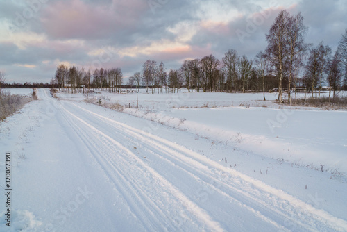 Winter morning, country road and fields covered with snow, in the distance you can see a hilly landscape.
