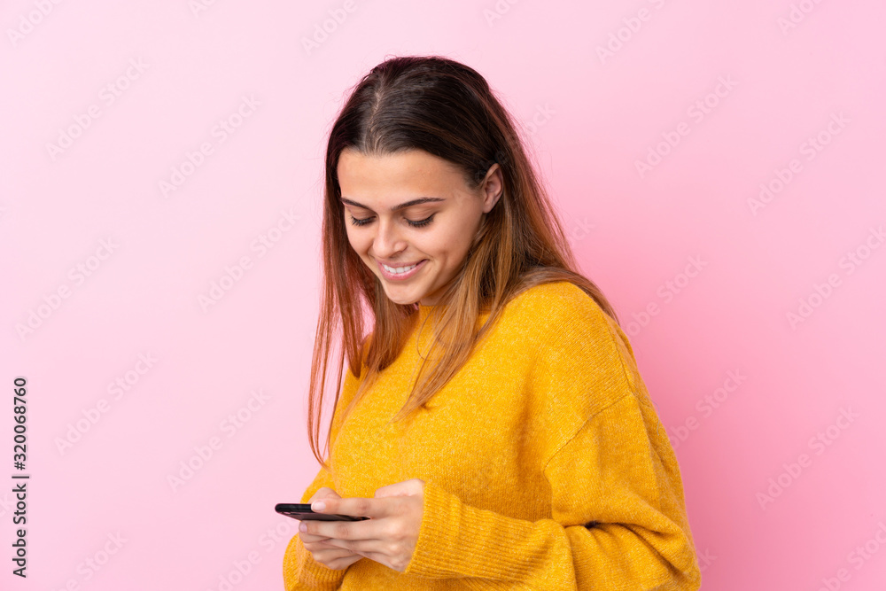 Teenager girl with yellow sweater over isolated pink background sending a message with the mobile Teenager girl with yellow sweater over isolated pink background sending a message with the mobile