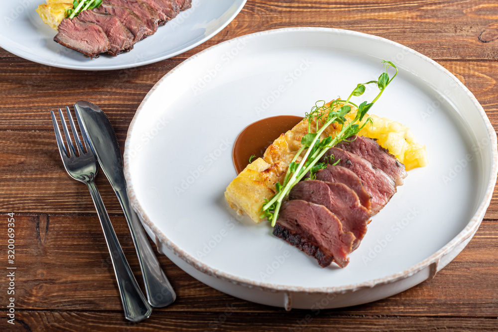Duck breast with a side dish of potato casseroles, seasoned with pea microgreen with tomato and chili sauce. On a white plate. On a wooden background, Duck breast with a side dish of potato casseroles, seasoned with pea microgreen with tomato and chili sauce. On a white plate. On a wooden background,