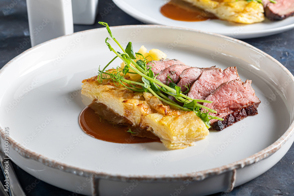 Duck breast with a side dish of potato casseroles, seasoned with pea microgreen with tomato and chili sauce. On a white plate. On a wooden background, Duck breast with a side dish of potato casseroles, seasoned with pea microgreen with tomato and chili sauce. On a white plate. On a wooden background,