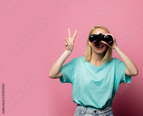 Beautiful smiling woman with binoculars on pink background