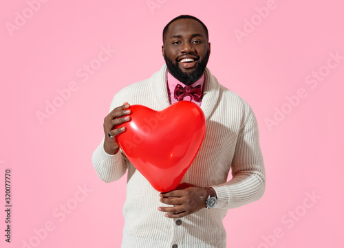 Happy man holds red heart shape balloon. Photo of handsome man in love on pink background © Romario Ien