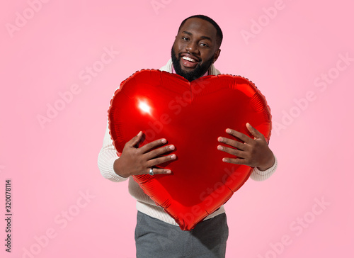 Happy man holds red heart shape balloon. Photo of handsome man in love on pink background. Valentine's Day © Romario Ien