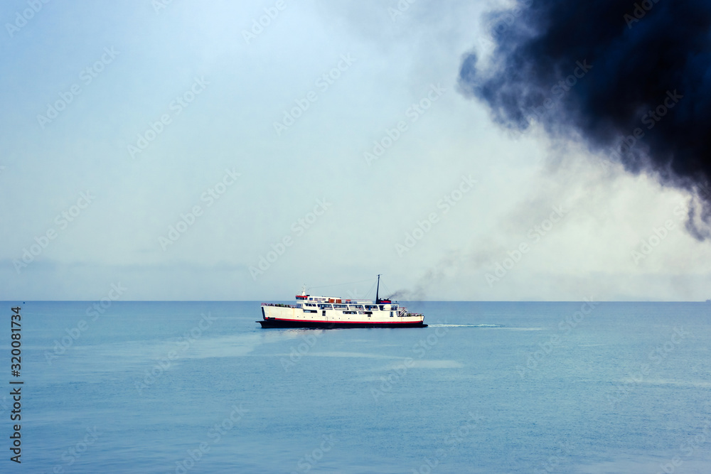 Exhaust pipe of ferry boat with black thick smoke coming out and sky with clouds on background. Air pollution.