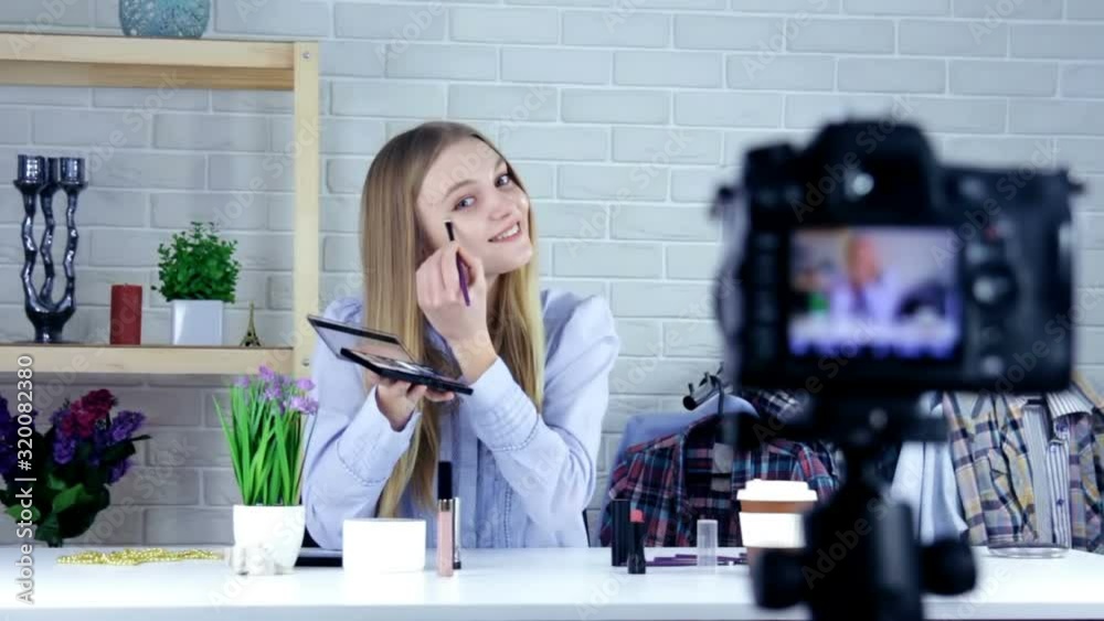 Smiling woman or beauty blogger with eye shadow brush, mirror and camera recording makeup tutorial video at home - blogging, technology, videoblog, makeup and people concept Smiling woman or beauty blogger with eye shadow brush, mirror and camera recording makeup tutorial video at home - blogging, technology, videoblog, makeup and people concept