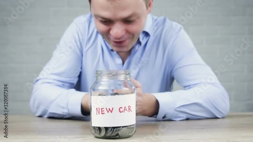 Man putting coins into jar with tag New Car. Saving money for new car concept : Coins in glass jars. Ideas of saving for a down payment on a car