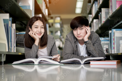 Portrait happy male and female student reading a book in the library