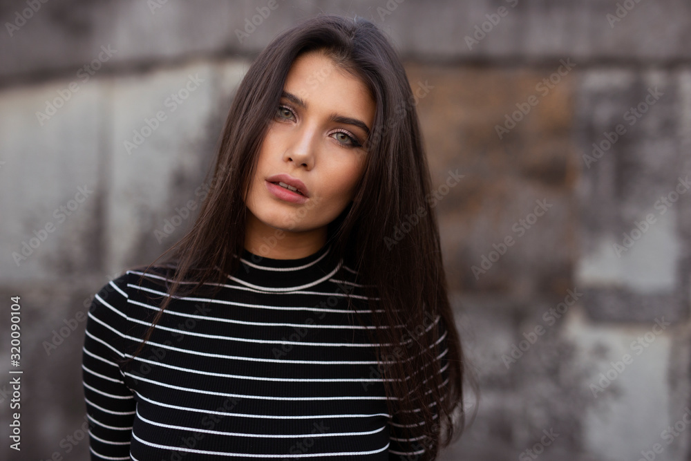 Horizontal view. Confident girl with straight brunette hair and makeup, looking confident at camera, over black old wall background.