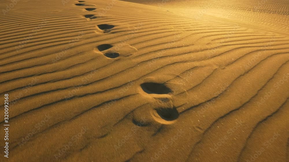 Footprints in the sand in desert at warm sunset lights. Сamera follows footprints in big sand dune. UHD, 4K