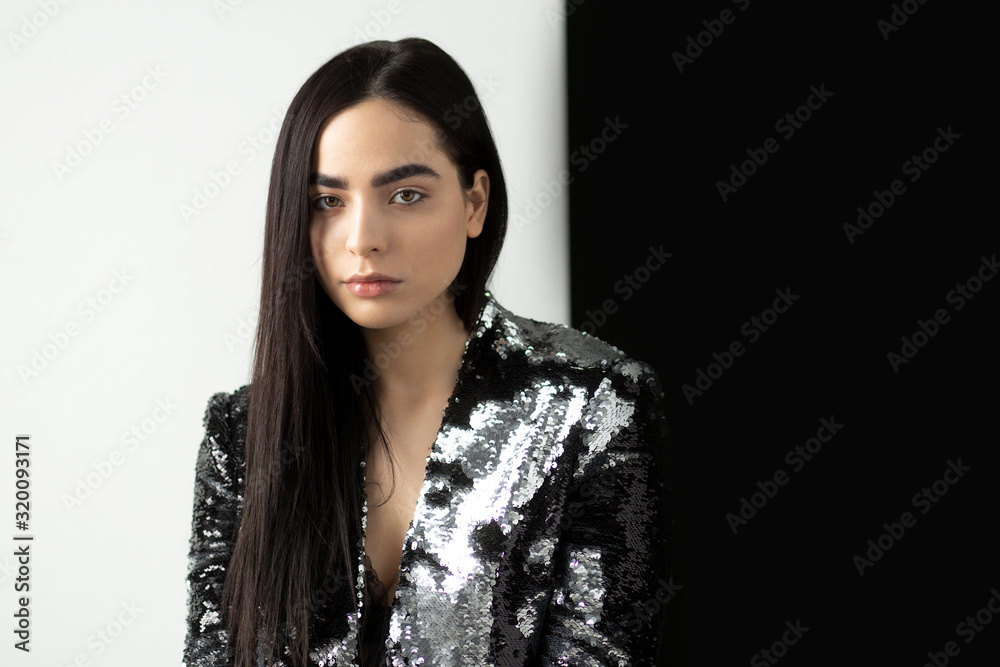 Portrait of a beautiful woman with a long brunette hair in a silver shiny jacket from sequins. Beautiful fashion model with natural makeup, eyebrows, isolated on white and black background. Portrait of a beautiful woman with a long brunette hair in a silver shiny jacket from sequins. Beautiful fashion model with natural makeup, eyebrows, isolated on white and black background.