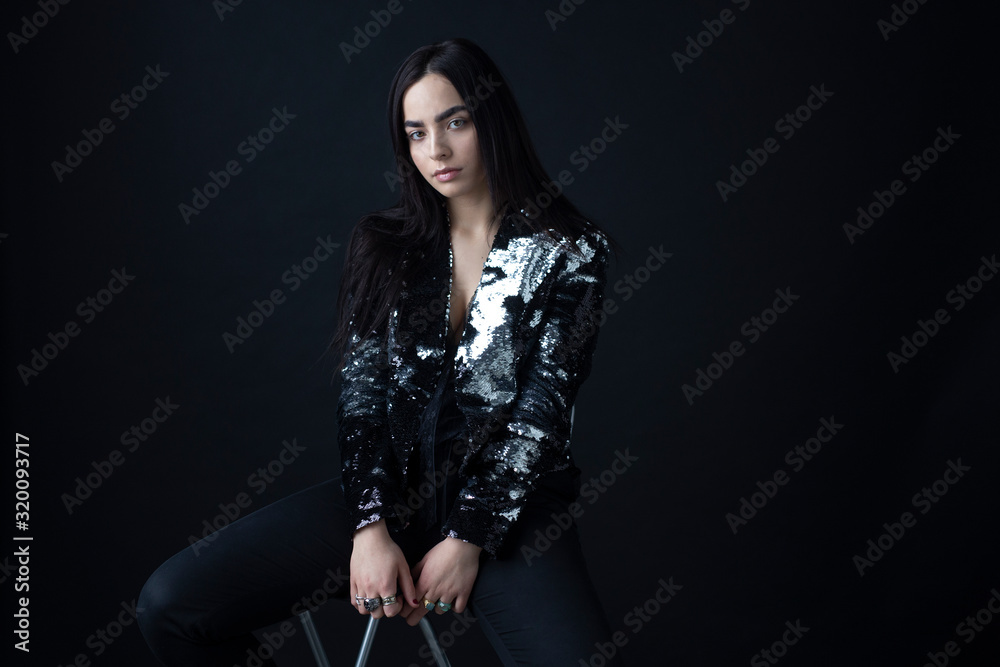 Fototapeta premium Woman with attitude, have long brunette hair in a silver shiny jacket from sequins, with natural makeup, eyebrows, over black background.
