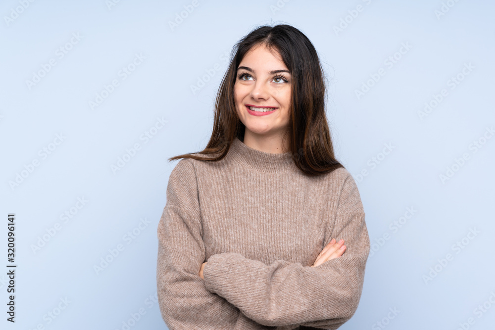 Young brunette woman wearing a sweater over isolated blue background looking up while smiling Young brunette woman wearing a sweater over isolated blue background looking up while smiling