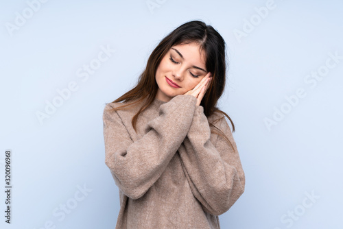 Young brunette woman wearing a sweater over isolated blue background making sleep gesture in dorable expression © luismolinero