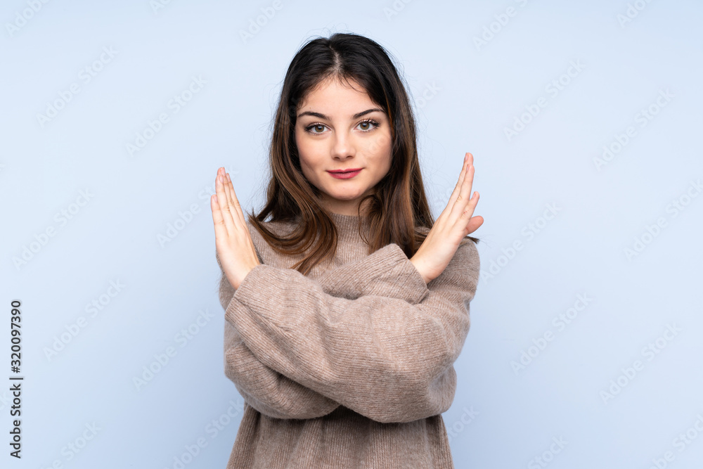 Young brunette woman wearing a sweater over isolated blue background making NO gesture Young brunette woman wearing a sweater over isolated blue background making NO gesture
