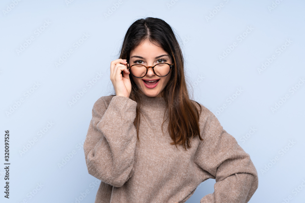 Young brunette woman wearing a sweater over isolated blue background with glasses and surprised