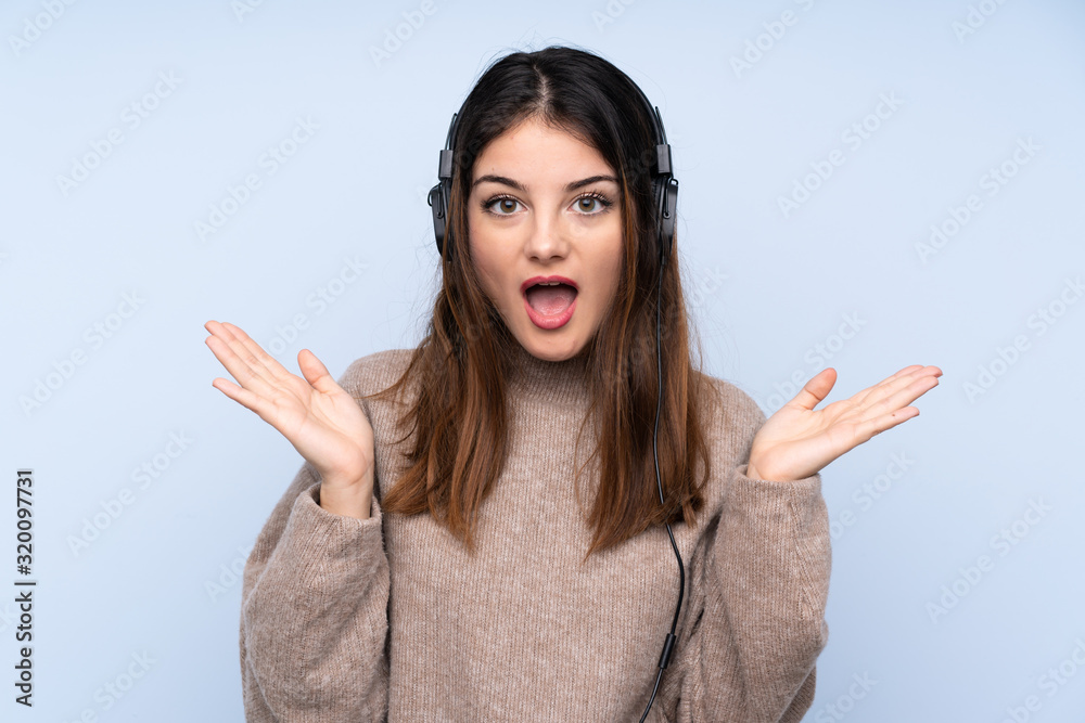 Young brunette woman over isolated blue background surprised and listening music Young brunette woman over isolated blue background surprised and listening music