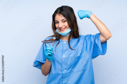Woman dentist holding tools over isolated blue background celebrating a victory
