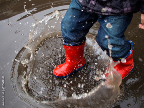 Obraz na plátně Low Section Of Child Wearing Rubber Boots Jumping In Puddle During Monsoon