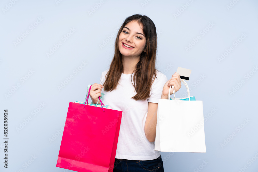 Young brunette woman over isolated blue background holding shopping bags and a credit card Young brunette woman over isolated blue background holding shopping bags and a credit card