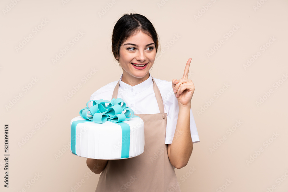 Pastry chef woman holding a big cake over isolated background intending to realizes the solution while lifting a finger up Pastry chef woman holding a big cake over isolated background intending to realizes the solution while lifting a finger up