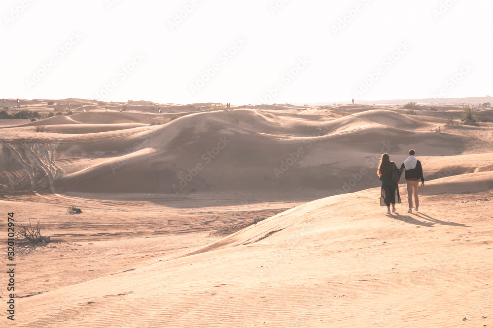 Young couple enjoying the sunset in dunes. Romantic traveler walking on the Sahara desert. Adventure travel lifestyle concept.