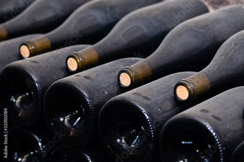 Stacks of wine bottles laying flat in racks in old wine cellar or cave. Concept vault with old rare wines, exclusive collection. Ancient wine bottles resting, aging, dusting in cellar