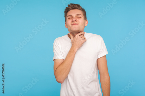 Sore throat, tonsillitis. Unhealthy flu-sick man in white t-shirt holding ill neck, suffering terrible throat pain, healthcare and medical concept. indoor studio shot isolated on blue background