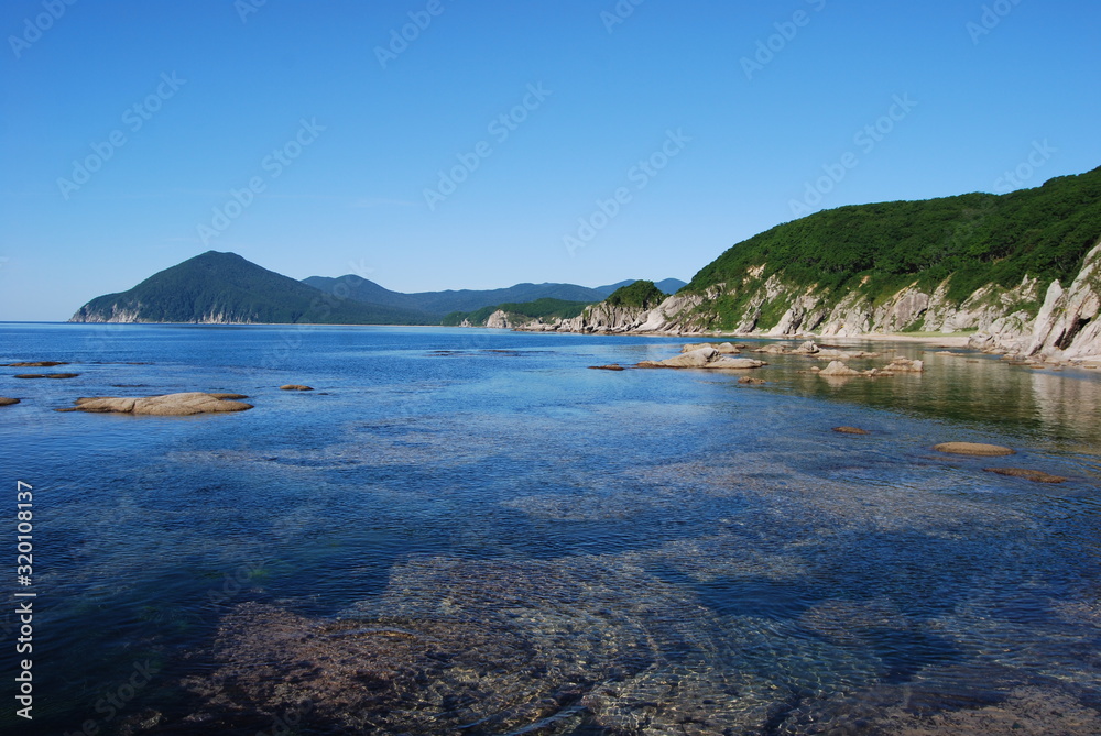 Calm waters of a bay. Rocky seashore of a Pacific Ocean. Saltwater inlet. Green hills by the sea. Rocks on the shallows.