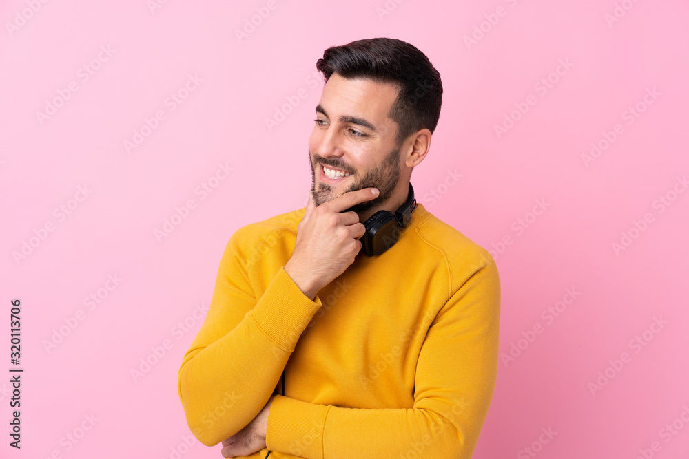 Young handsome man with earphones over isolated pink background looking side Young handsome man with earphones over isolated pink background looking side
