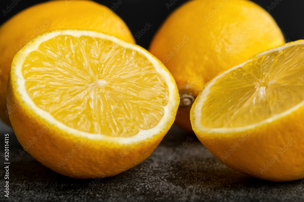 Close-up of yellow lemons, one is halved. Placed on a dark gray concrete surface. Close-up of yellow lemons, one is halved. Placed on a dark gray concrete surface.