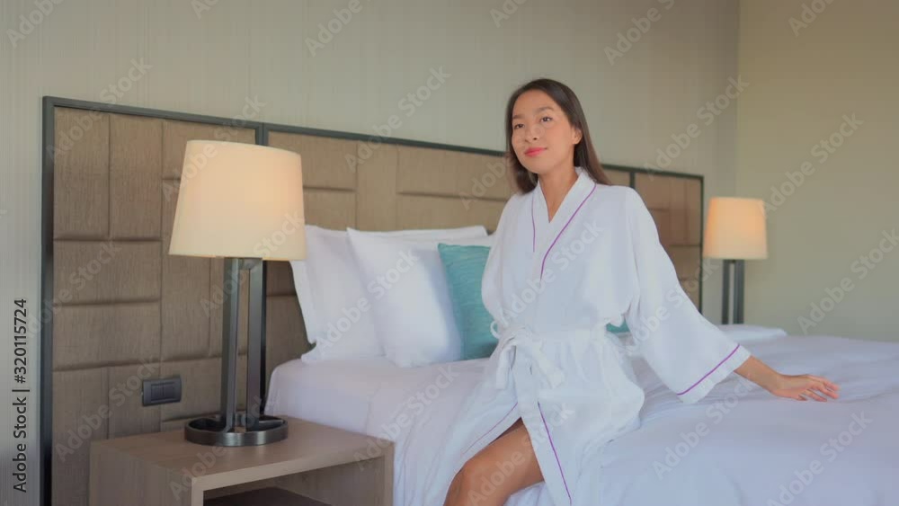 An attractive young Asian woman dressed in a hotel resort robe leans back on the bed in her room. An attractive young Asian woman dressed in a hotel resort robe leans back on the bed in her room.