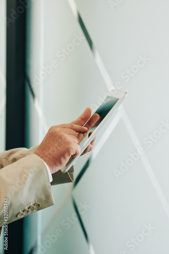 Vertical shot of unrecognizable mature man wearing suit working on tablet PC