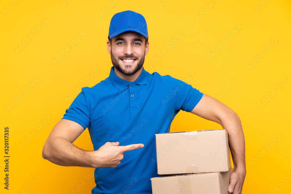 Delivery man over isolated yellow background and pointing it Delivery man over isolated yellow background and pointing it